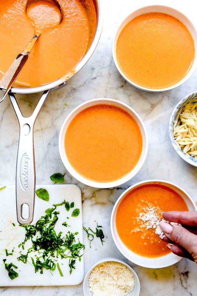 garnishing bowls of tomato basil soup with Parmesan cheese