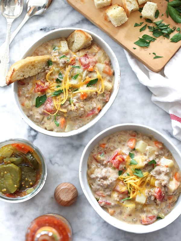 two bowls of cheeseburger soup next to jar of pickles