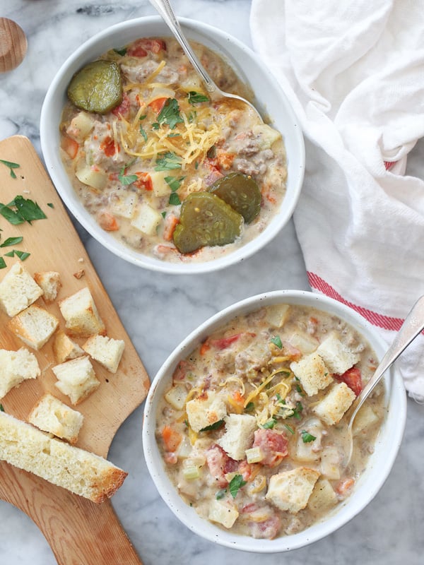 two bowls of cheeseburger soup garnished with croutons and pickles