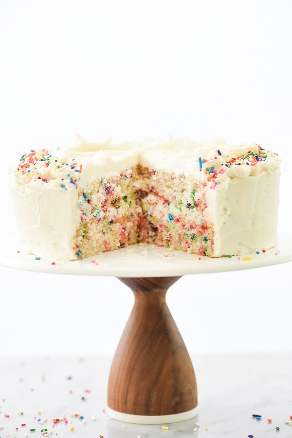 sliced confetti cake on cake stand frosted with homemade buttercream frosting