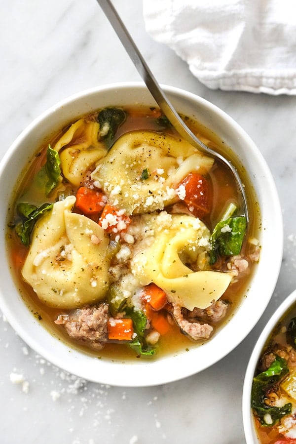 bowl of sausage and tortellini soup garnished with parmesan