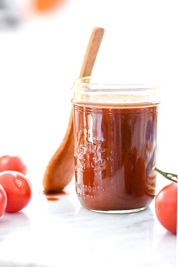 red enchilada sauce in glass jar with wooden spoon