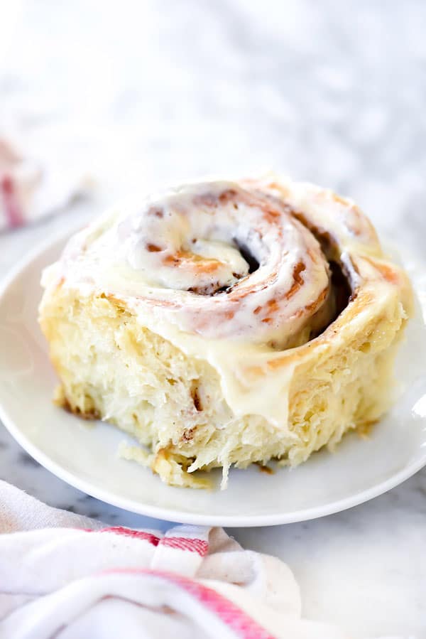 single homemade cinnamon rolls slathered with frosting on white plate