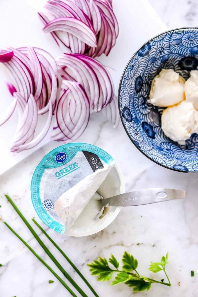 container of greek yogurt next to sliced red onion on counter