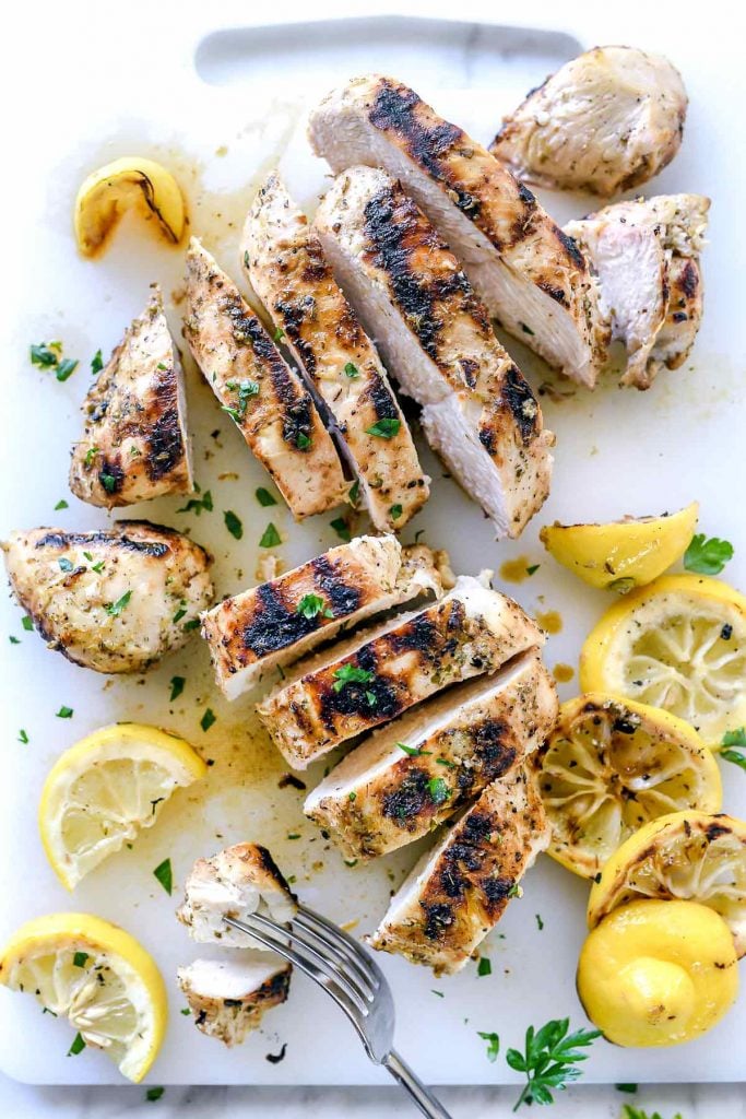 Sliced Greek chicken breasts on cutting board with lemons 