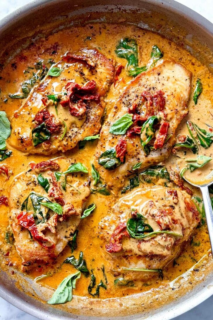 Easy Marry Me Chicken Recipe chicken breast in creamy sun-dried tomato sauce in skillet with spoon foodiecrush.com