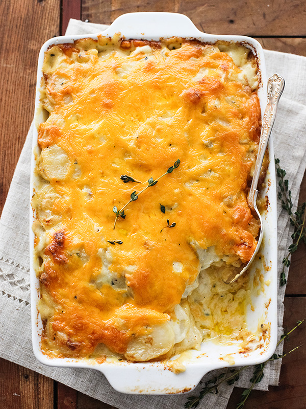 easy cheesy scalloped potatoes in white baking dish with spoon
