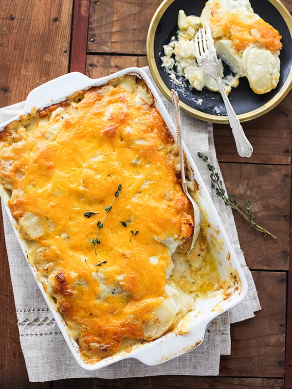 cheesy scalloped potatoes in white baking dish next to plate with single serving