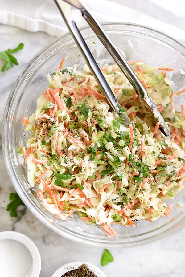 creamy coleslaw in a large glass bowl with metal tongs