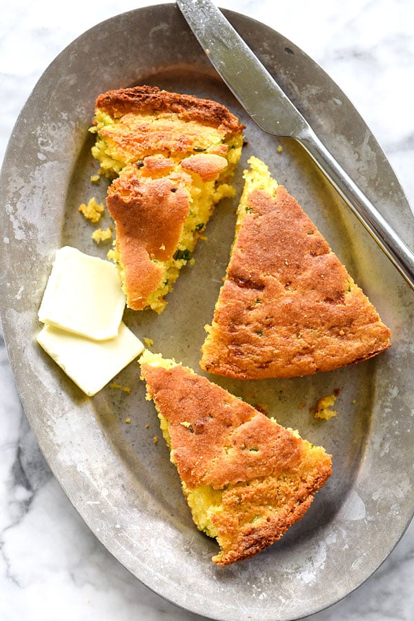 three slices of jalapeno cornbread on silver plate with knife and pats of butter