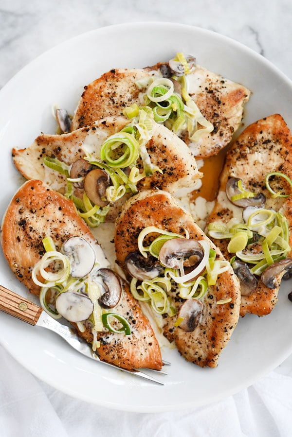 chicken with mushroom sauce and leeks on white plate with fork