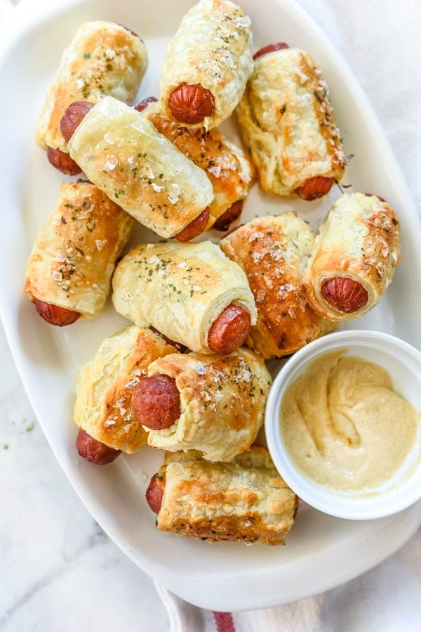 puff pastry pigs in a blanket on a white serving platter with mustard