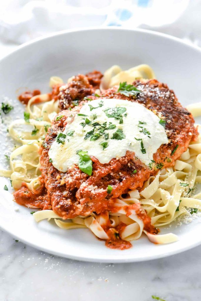 chicken parm on white plate with buttered noodles