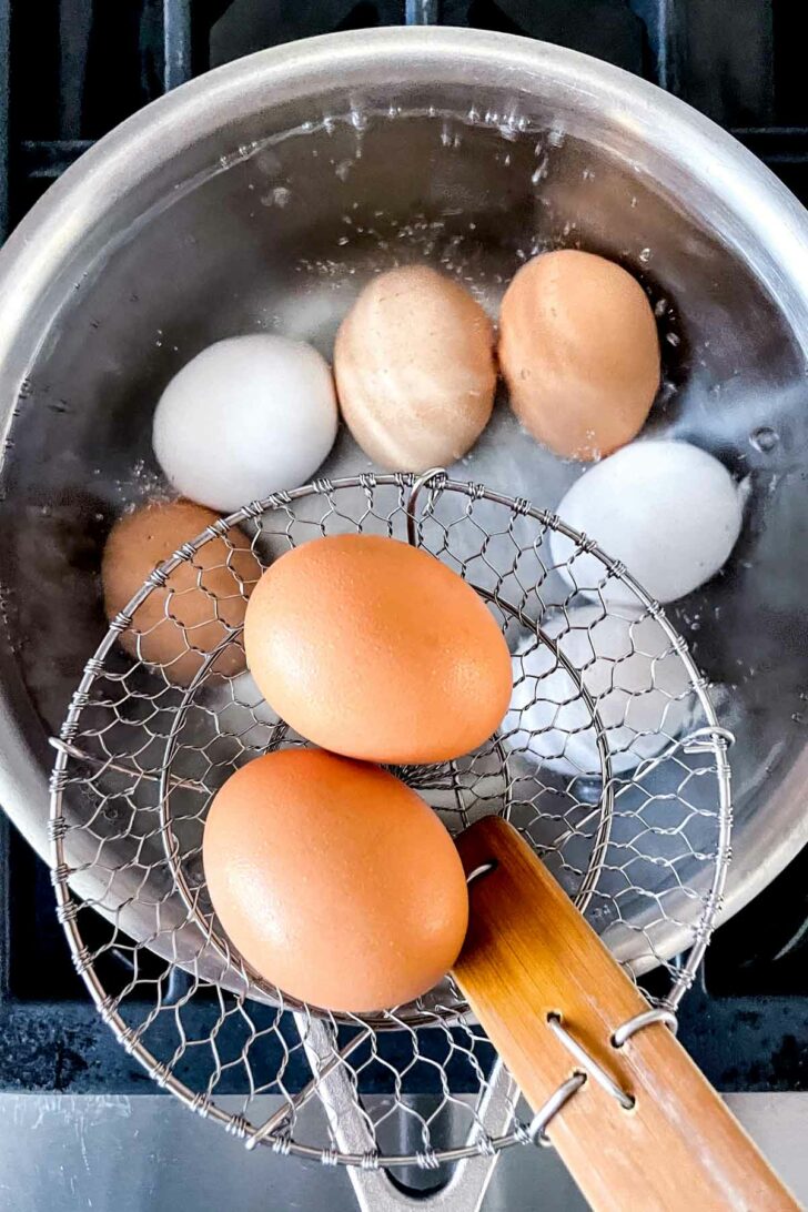 Eggs in spider strainer going into boiling water in pan foodiecrush.com
