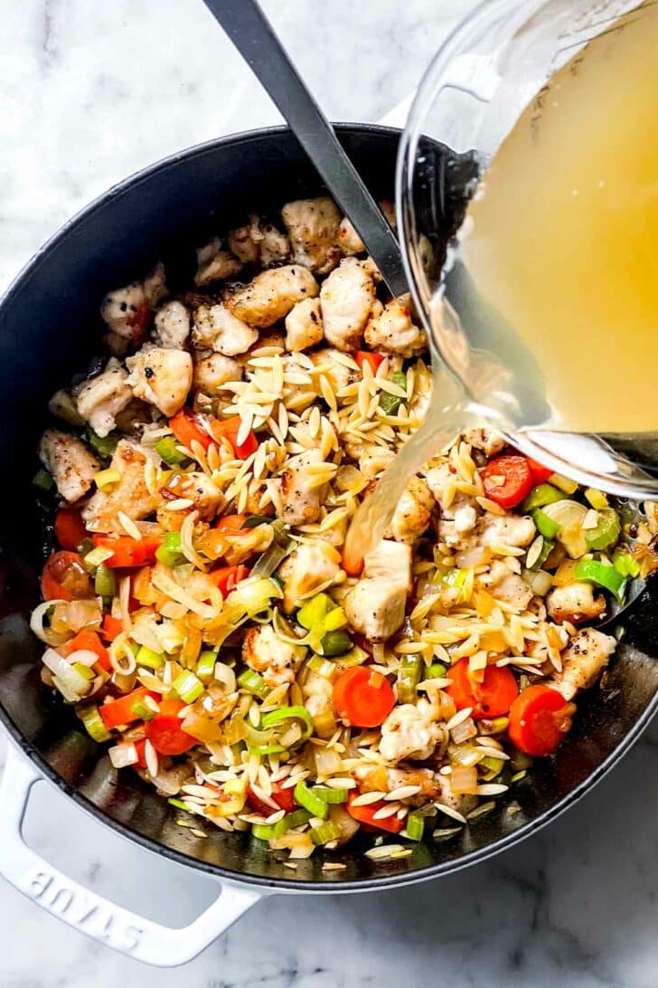 Stock poured over chicken with orzo, leek, carrots and onion in dutch oven foodiecrush.com