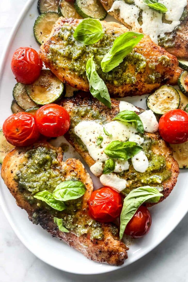 Pesto Chicken Recipe with mozzarella on platter with tomatoes and zucchini foodiecrush.com