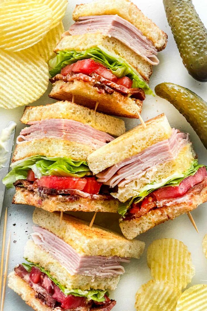 Club Sandwich with toothpicks on plate with potato chips and pickles foodiecrush.com