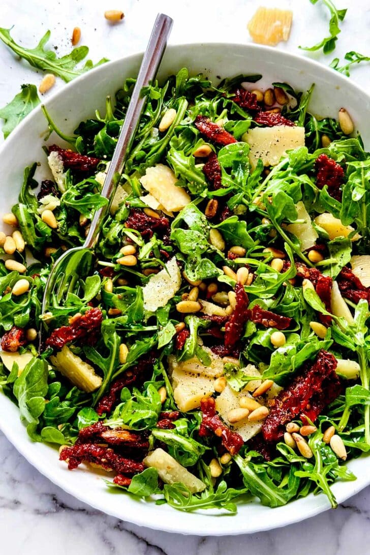 Arugula Salad with Sun Dried Tomatoes and Pine Nuts Salad in bowl with fork foodiecrush.com #arugulasalad