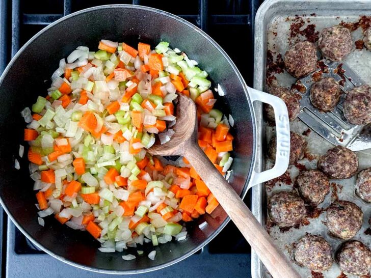 Cooked meatballs on baking sheet with onions carrot and celery in dutch oven for Italian Wedding Soup recipe foodiecrush.com