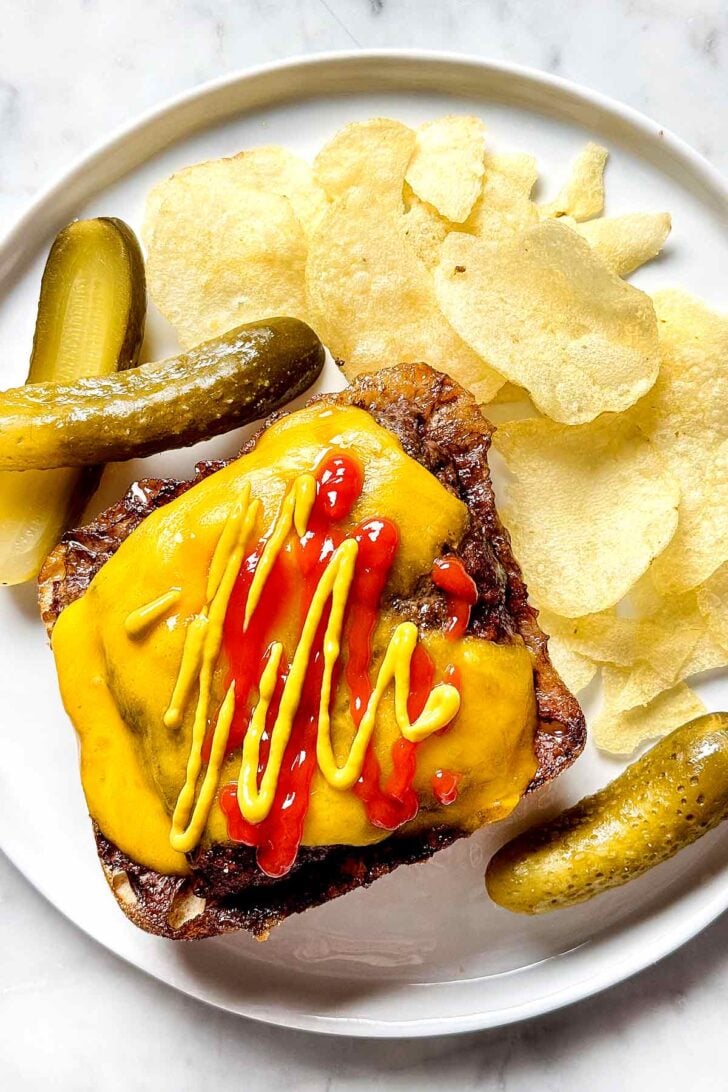 Baked Hamburger with cheese on plate with chips and pickles