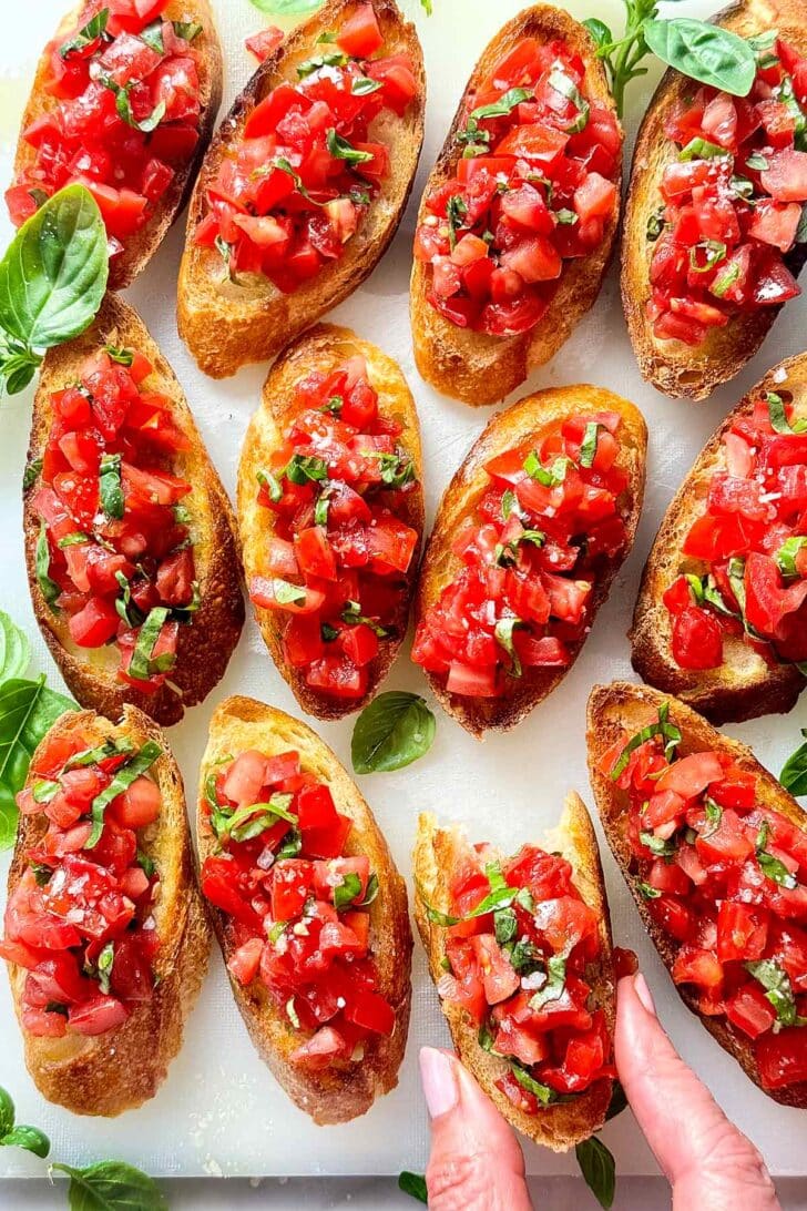 A bruschetta toast being taken off of a plate 