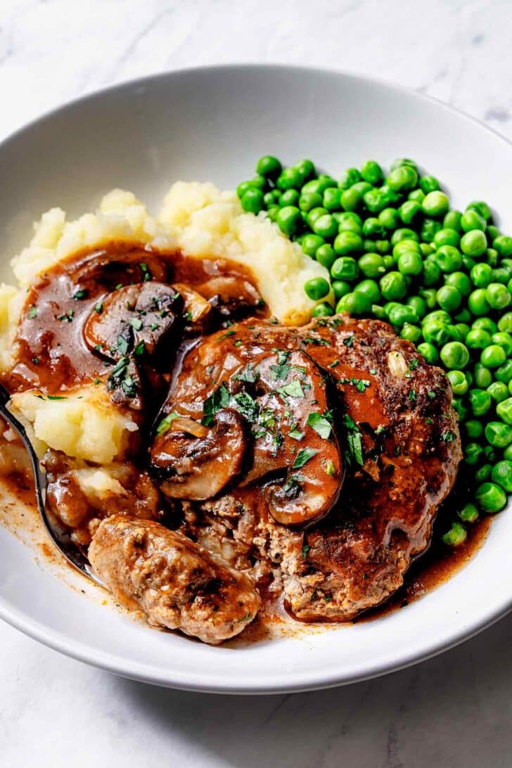 Salisbury Steak recipe with mushroom gravy with mashed potatoes and green peas on plate