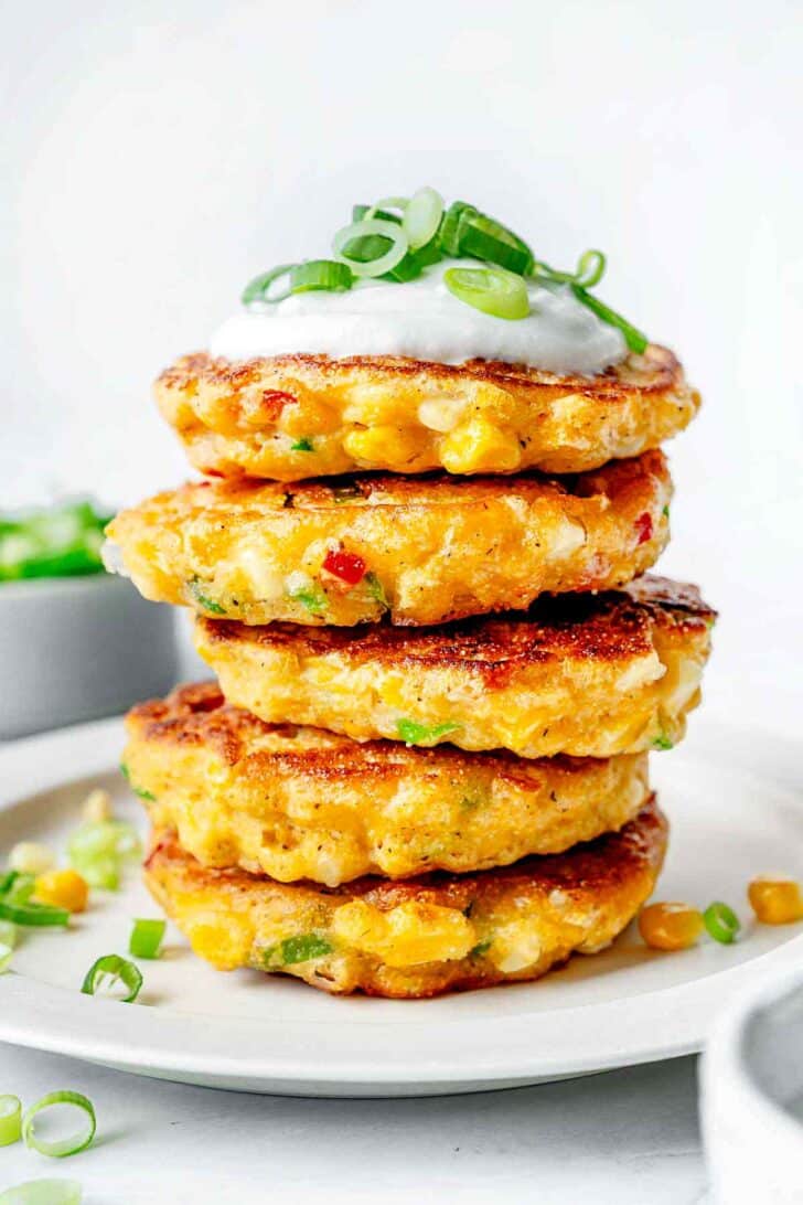 Stack of What's in Corn Fritters recipe with sour cream and green onions on plate